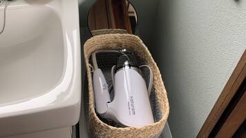 A bathroom with a white sink, a mirror, a white electric toothbrush in a woven basket, and a power outlet on the wall.