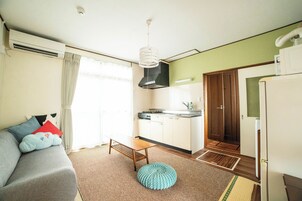 Un espacio habitable compacto con sofá, una mesita, una zona de cocina y una puerta que da a otra habitación.