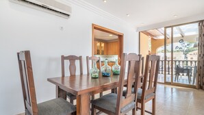 A dining area with a wooden table and chairs, a kitchen in the background, and a view through a glass door. - Cozy Apartment 3 Minutes from the Beach with Air Conditioning, Terrace & Garden (Alcudia)