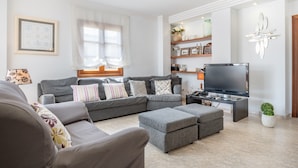 A living room with a sectional sofa, ottomans, a flat-screen TV, and a decorative wall piece. - Cozy Apartment 3 Minutes from the Beach with Air Conditioning, Terrace & Garden (Alcudia)