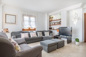 Un salon comprenant un canapé d’angle, des poufs, un téléviseur à écran plat et un élément décoratif mural.