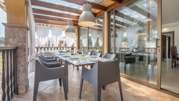 A dining area with a table set for four, a glass partition, and a view of the outdoor patio. - Cozy Apartment 3 Minutes from the Beach with Air Conditioning, Terrace & Garden (Alcudia)