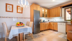 A kitchen with wooden cabinets, a stainless steel refrigerator, a dining table with a fruit bowl, and a chandelier. - Cozy Apartment 3 Minutes from the Beach with Air Conditioning, Terrace & Garden (Alcudia)