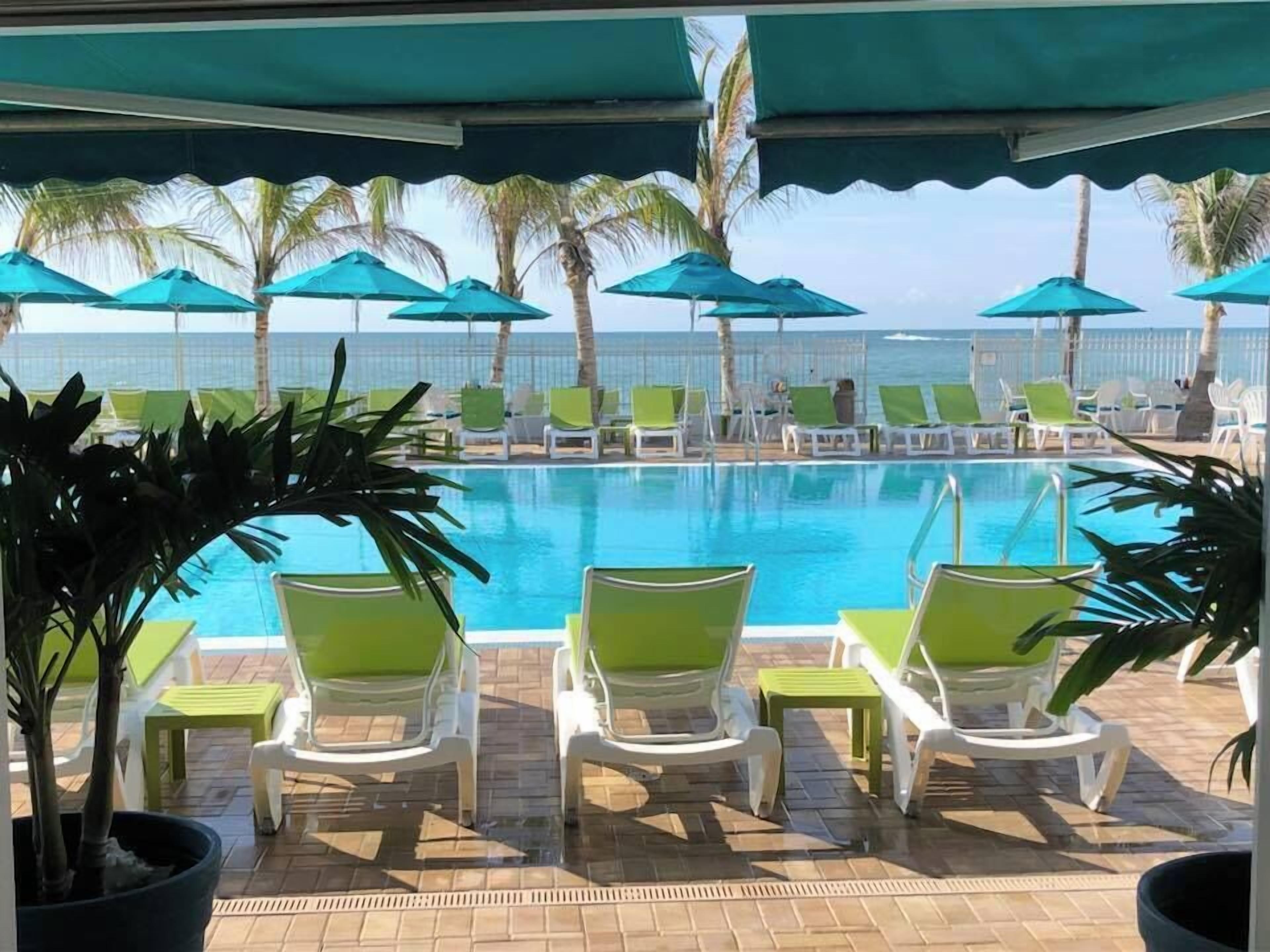A poolside area with lounge chairs and umbrellas, overlooking the ocean.