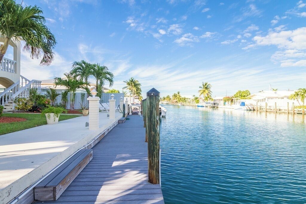 A waterfront property with a wooden dock, palm trees, and a clear blue sky.