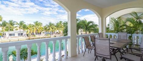 A covered outdoor area with a table and chairs, overlooking a pool and palm trees.