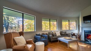 A spacious living room with large windows, a fireplace, and a variety of seating options. - Tree House in Center of Helen (Helen)