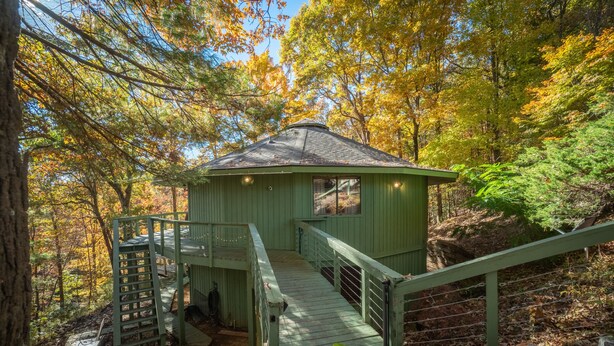 A green wooden cabin with a wooden staircase leading to a deck, surrounded by autumn foliage. - Tree House in Center of Helen (Helen)