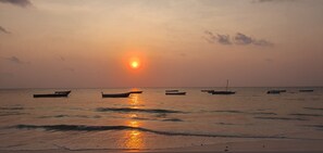 Una playa con barcos y el sol poniéndose sobre el agua.