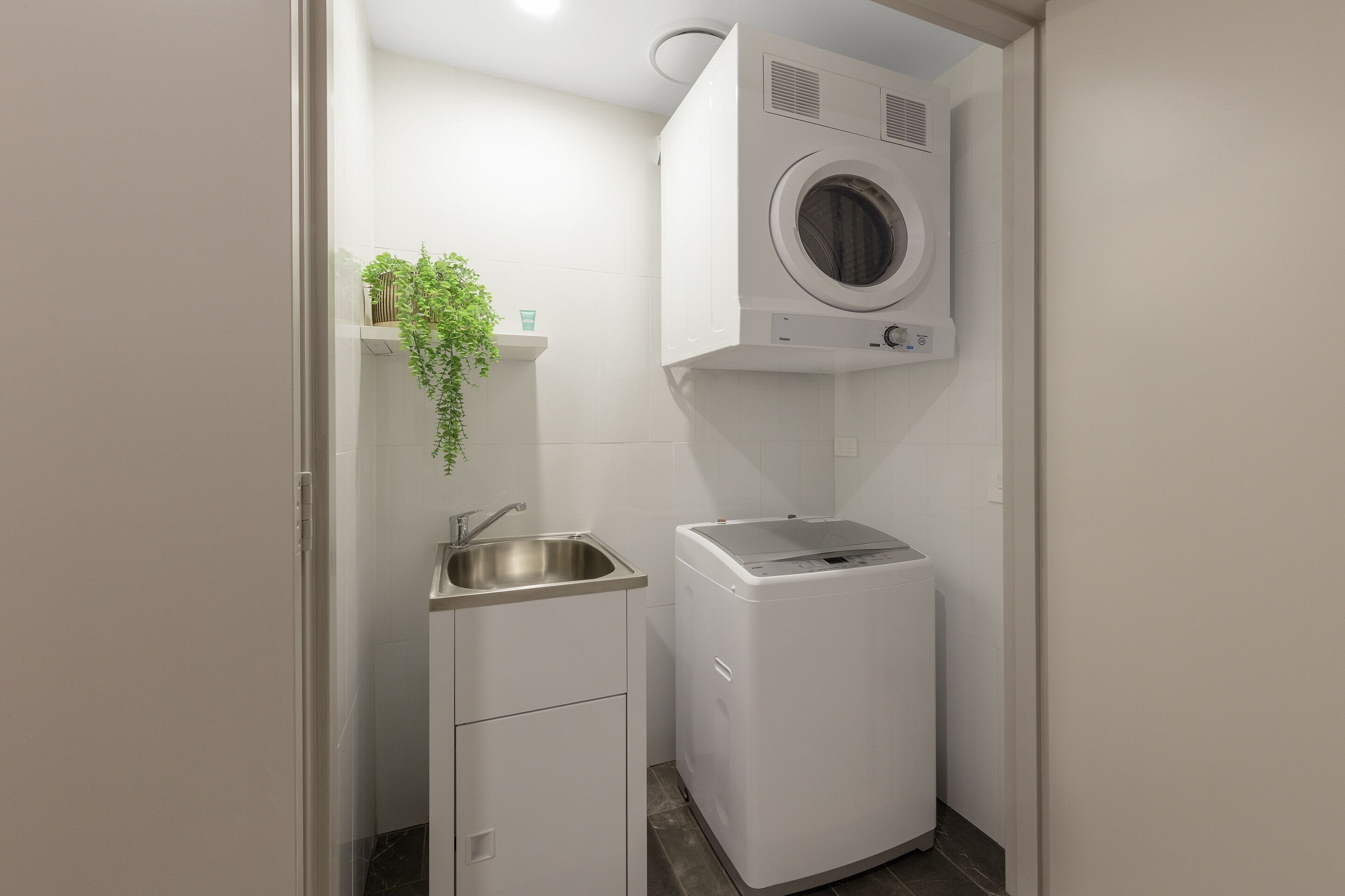 Une petite buanderie comprenant un lave-linge, un évier et un petit meuble de rangement.