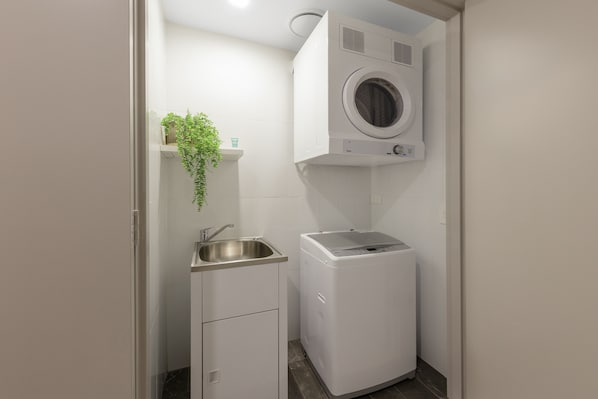 A compact laundry room with a washing machine, a sink, and a small cabinet. - Meriton Suites Surfers Paradise (Surfers Paradise)
