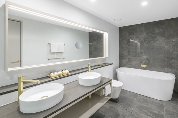 Un baño moderno con dos lavamanos, un espejo grande y una bañera independiente.