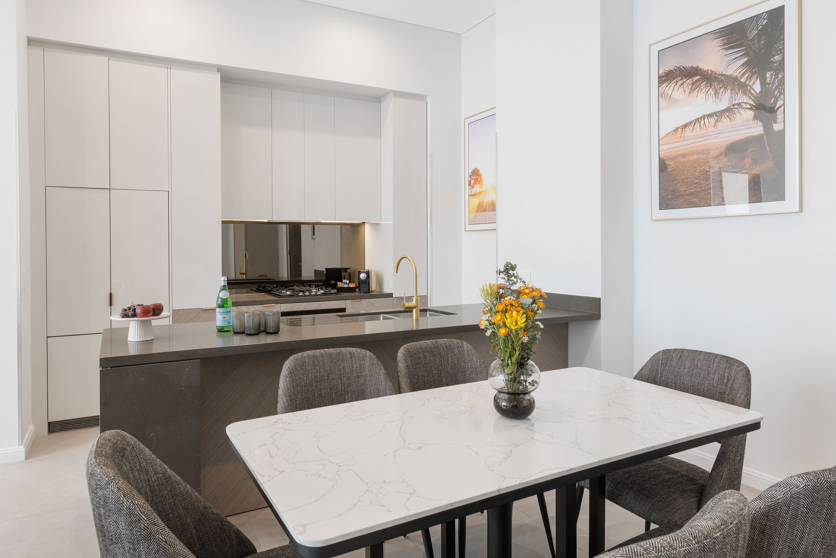 Une cuisine moderne avec des meubles blancs, un îlot central et un coin repas comprenant une table en marbre et des chaises grises.