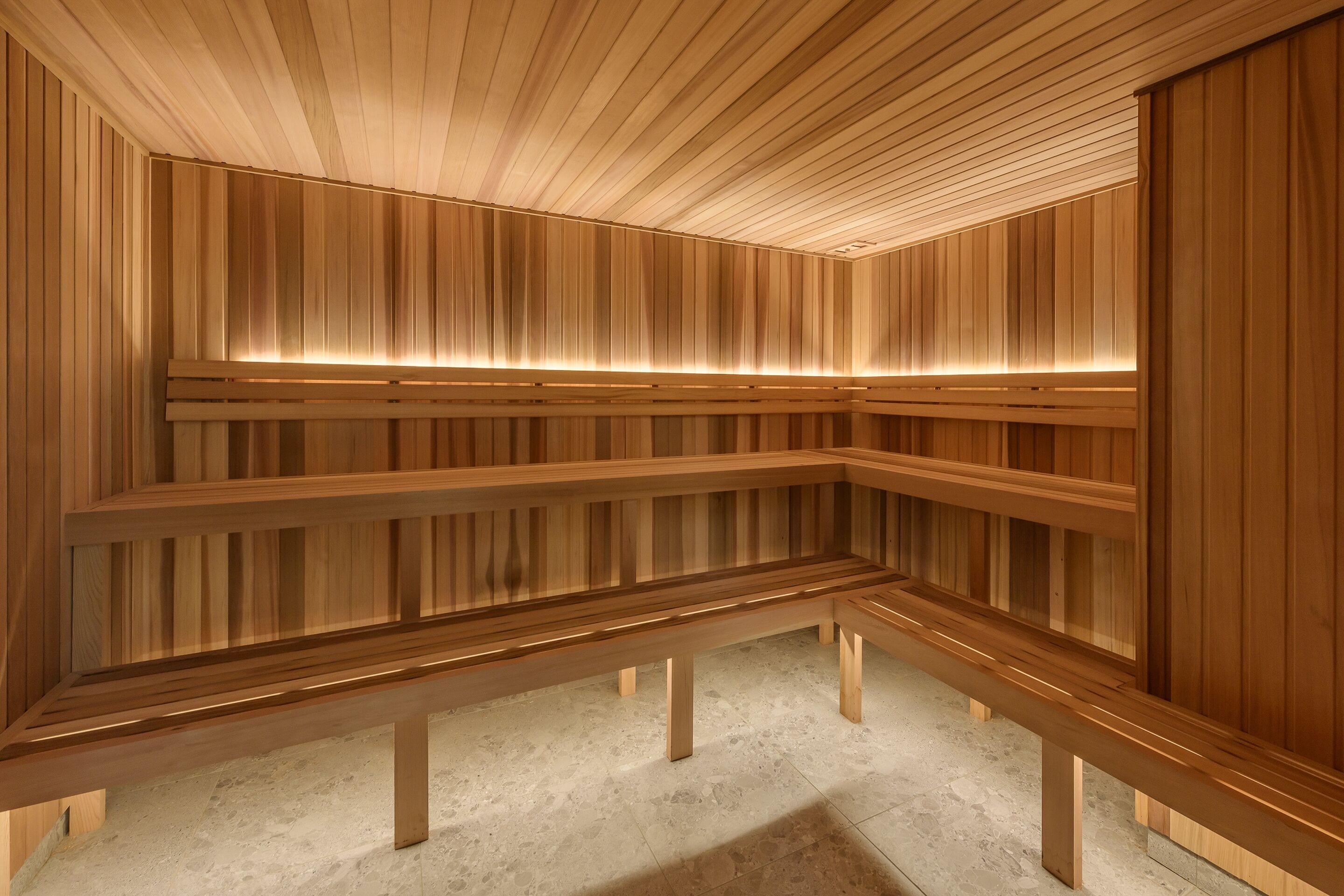 Un sauna avec des bancs en bois et des parois à lattes, éclairé par une lumière chaleureuse.