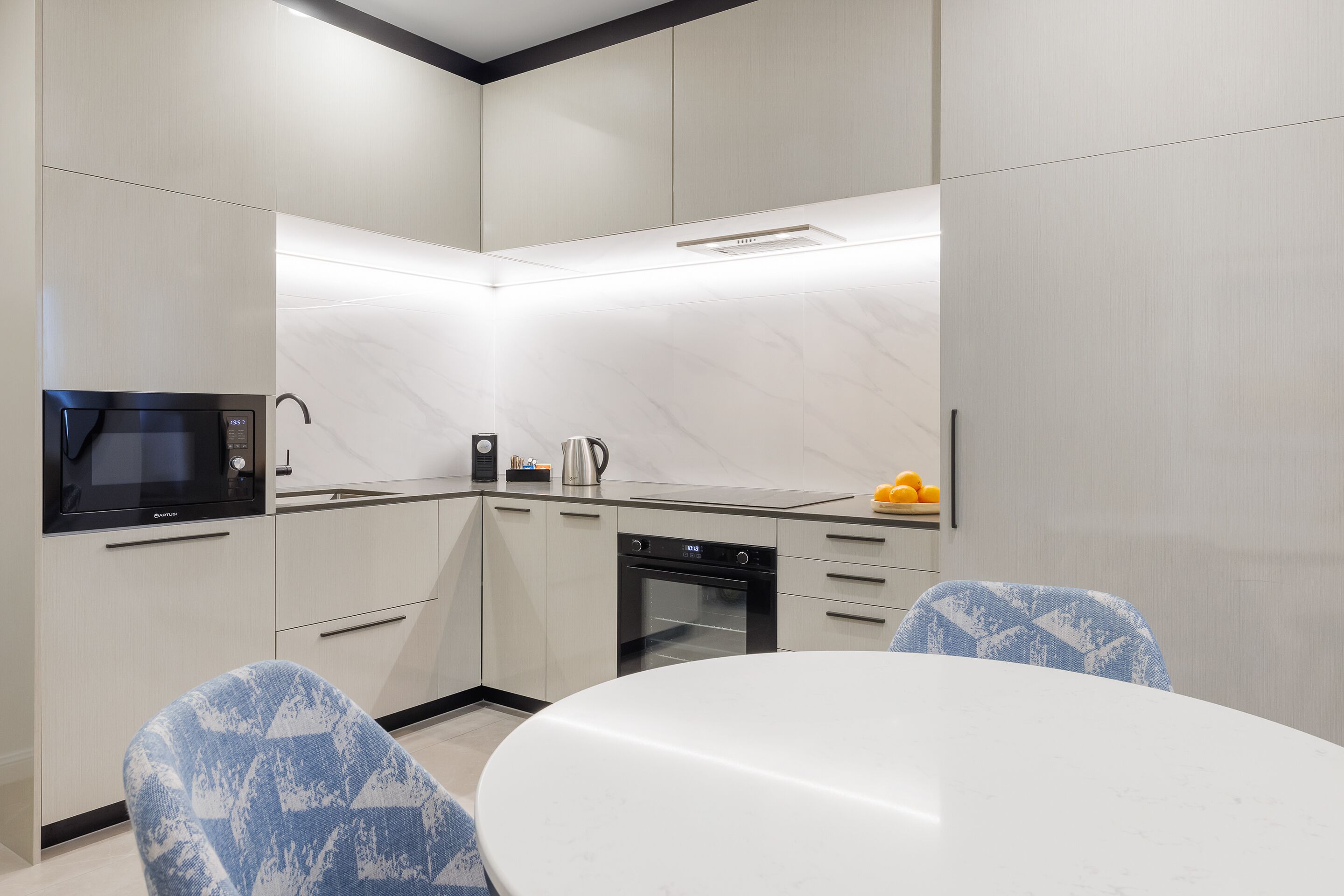 A modern kitchen with a microwave, oven, and sink. There is a dining table with chairs.