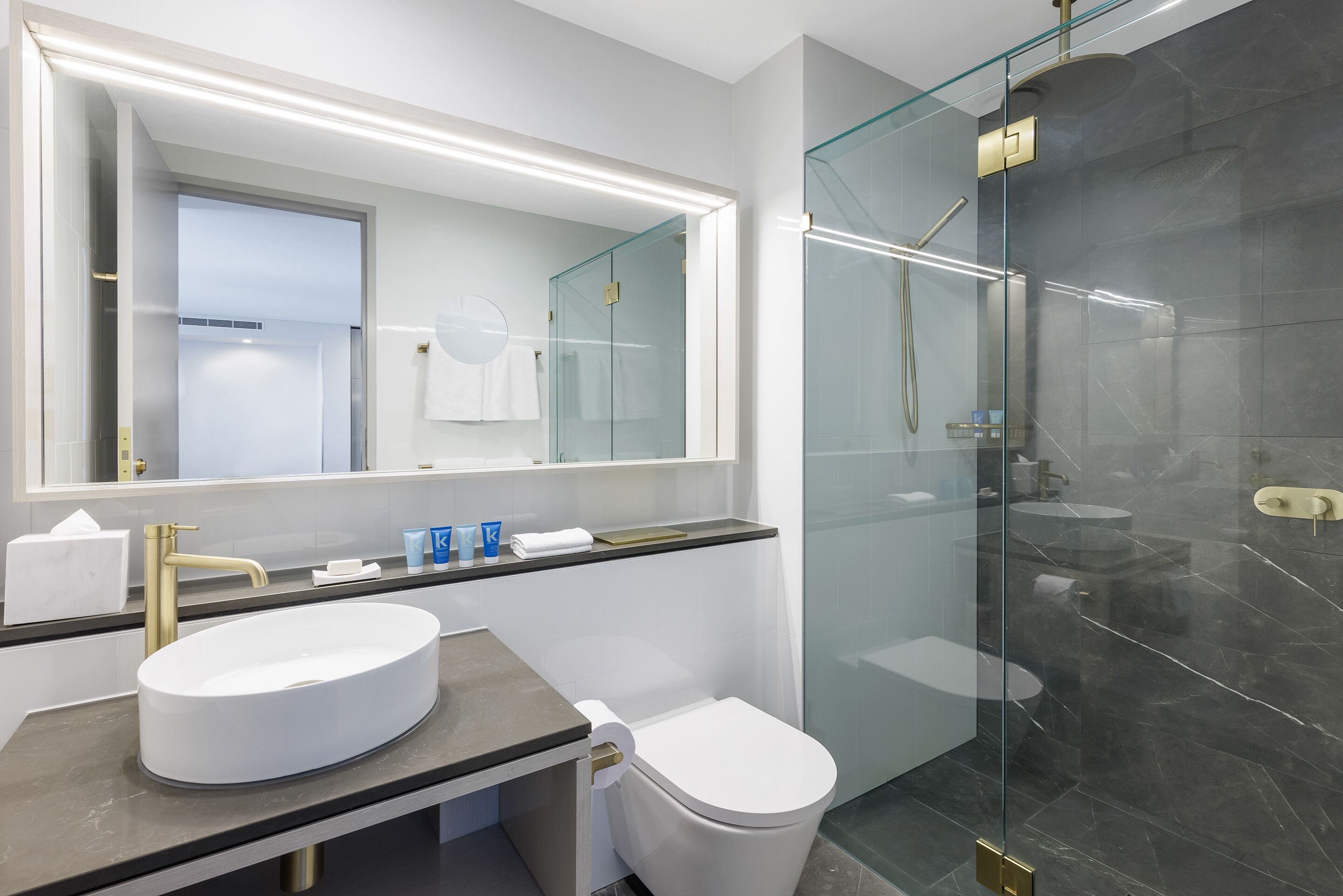 A modern bathroom with a large mirror, a round sink, a toilet, and a glass-enclosed shower area.