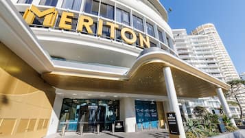 Entrada de un hotel con un llamativo cartel de 'Meriton', un diseño arquitectónico moderno y cielo despejado.