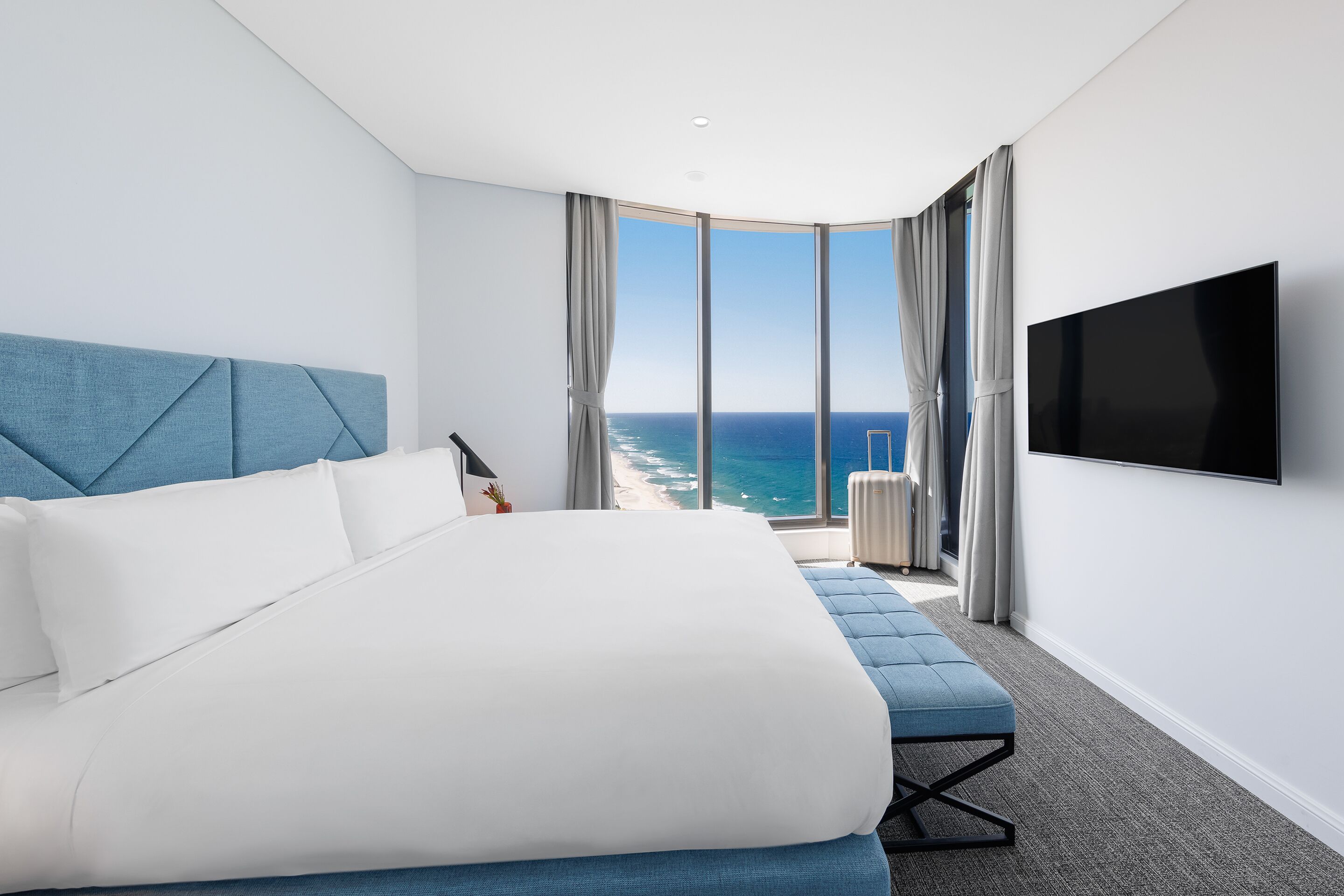 Une chambre d’hôtel moderne dotée d’un grand lit, d’une télévision à écran plat, d’une vue sur l’océan et d’un balcon avec des rideaux.