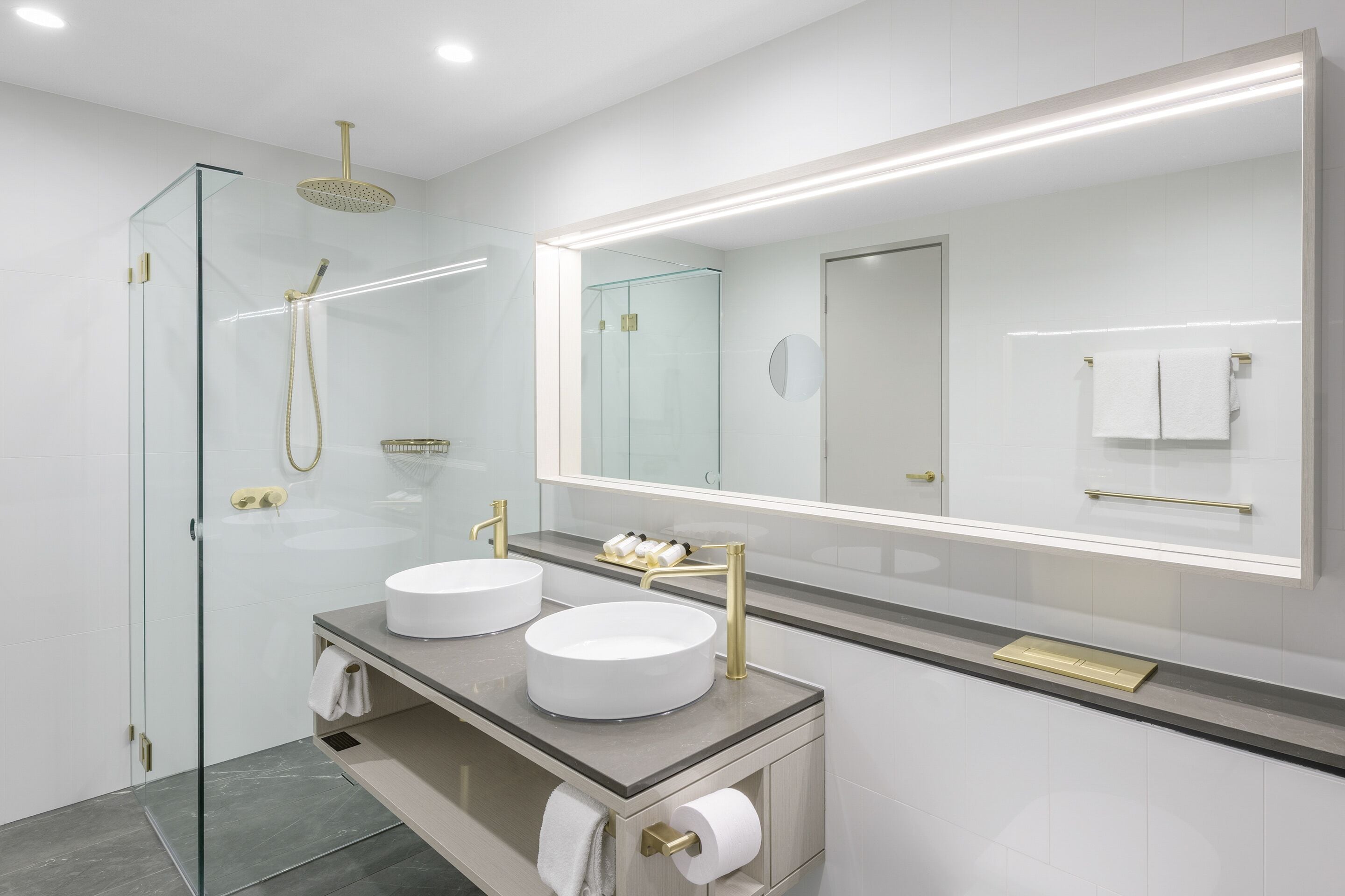 Un baño moderno con dos lavamanos, cabina de ducha de cristal y un espejo grande.