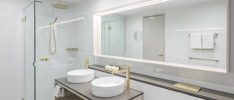 Un baño moderno con dos lavamanos, cabina de ducha de cristal y un espejo grande.