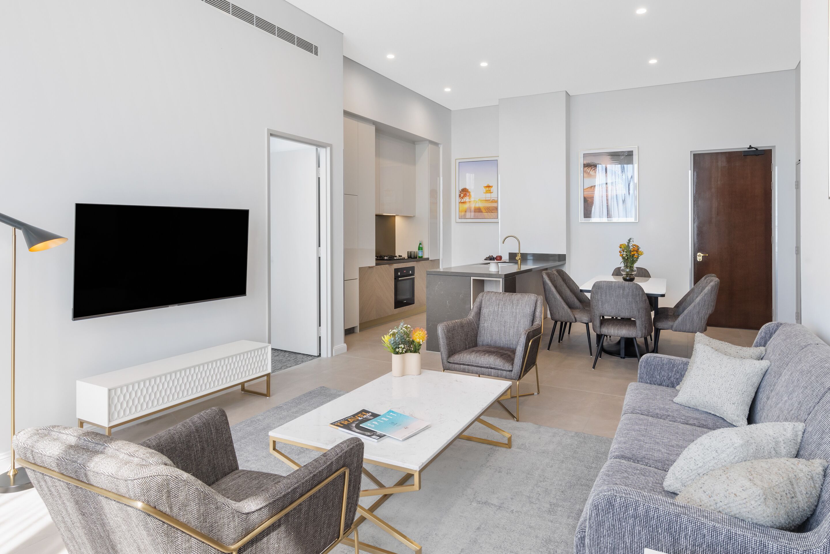 A modern living room with a flat-screen TV, a white coffee table, and grey sofas.