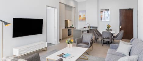 A modern living room with a flat-screen TV, a white coffee table, and grey sofas.