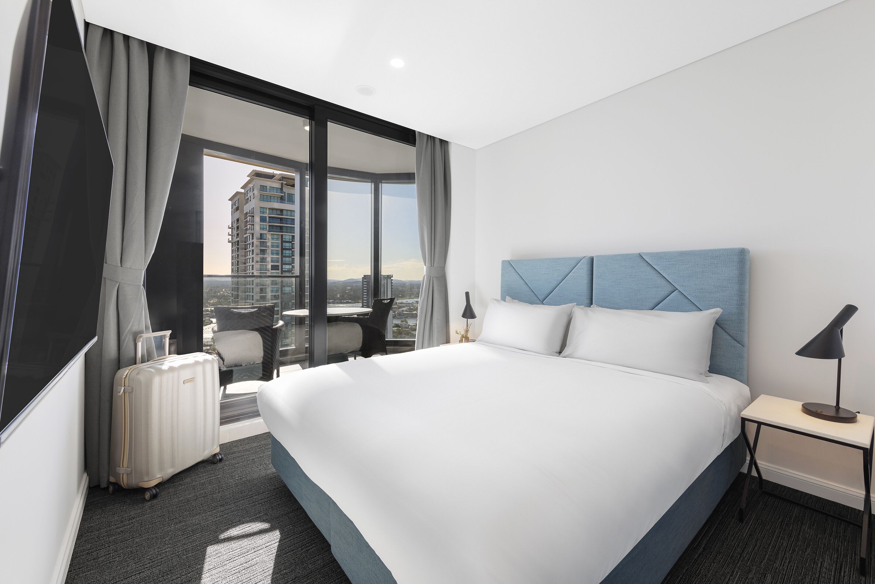 A modern hotel room with a large bed, a desk, and a view of the city.
