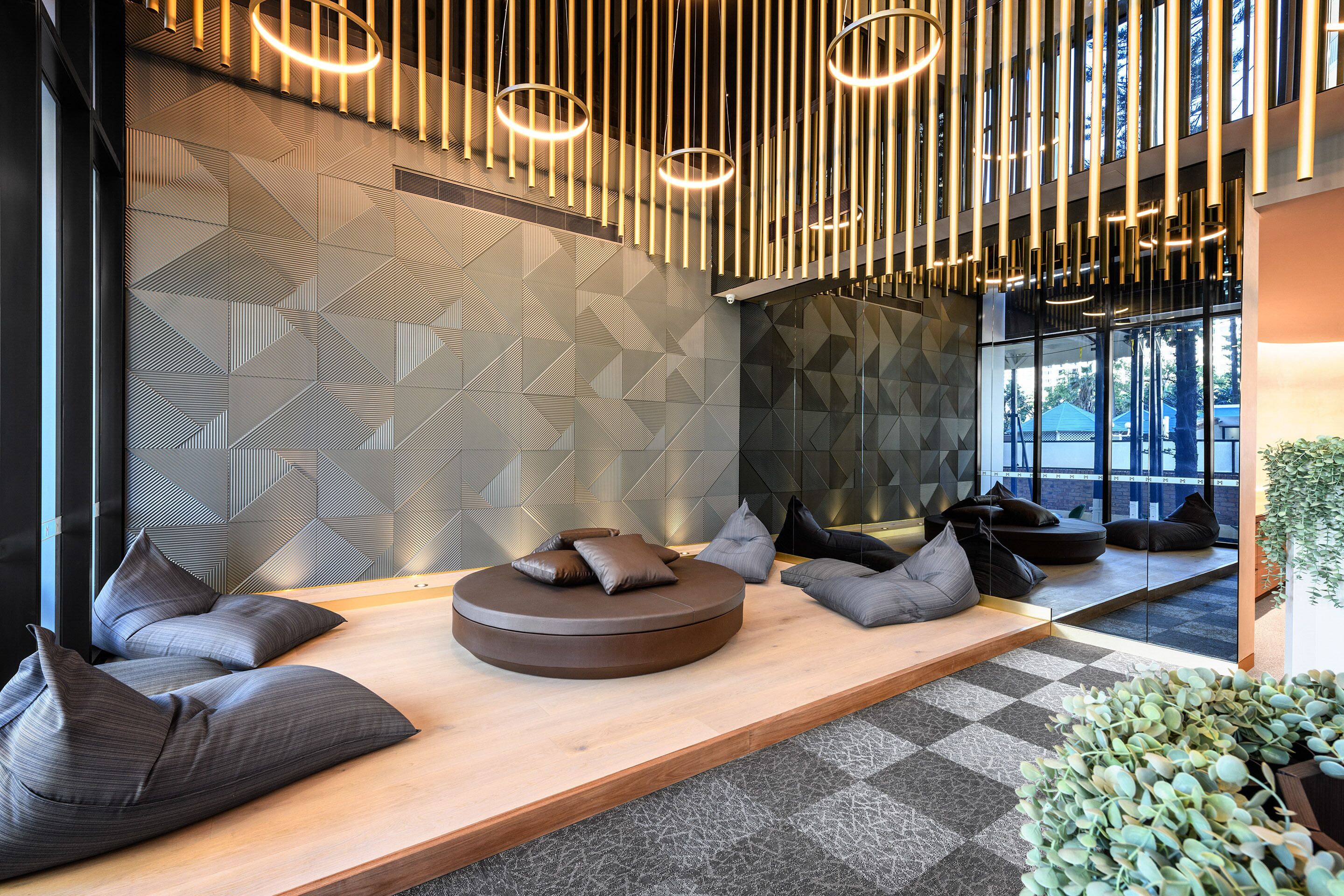 A modern interior with a wooden bench, grey cushions, and a geometric patterned wall.