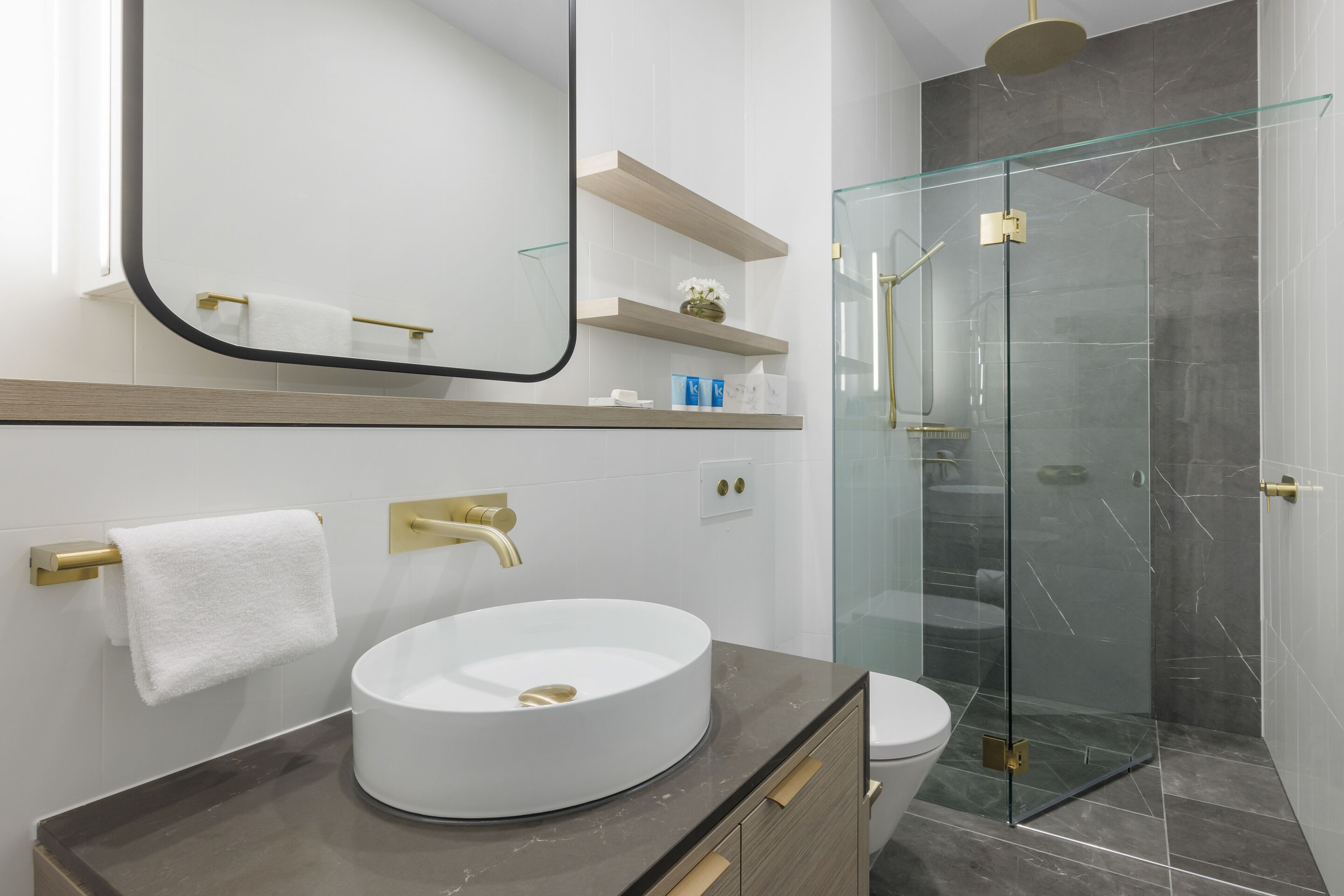 Un bagno moderno con un lavandino bianco rotondo, un rubinetto dorato, un box doccia in vetro e un water.
