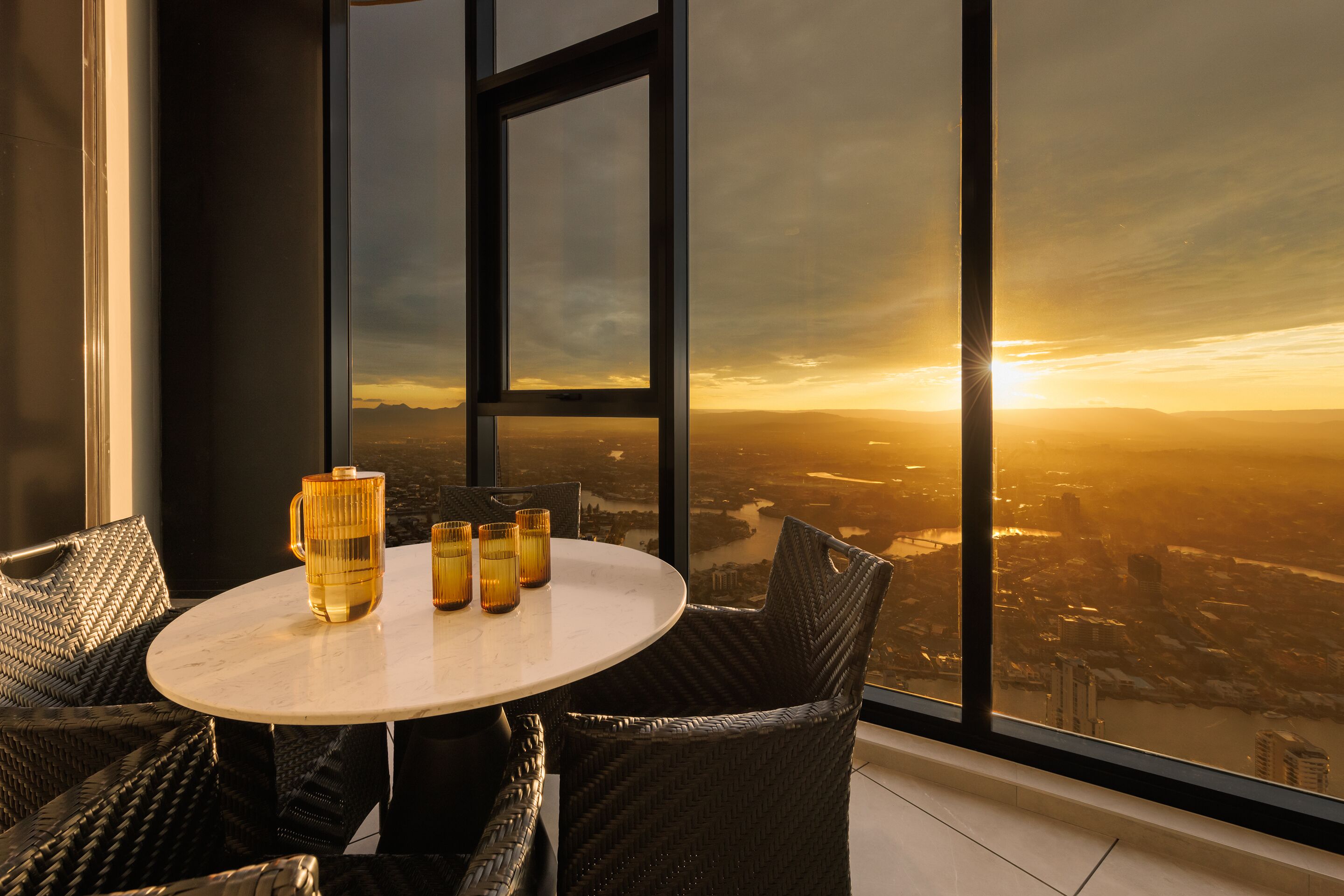 Une chambre située dans un immeuble de grande hauteur, dotée d’une grande fenêtre donnant sur une vue panoramique de la ville au coucher du soleil.