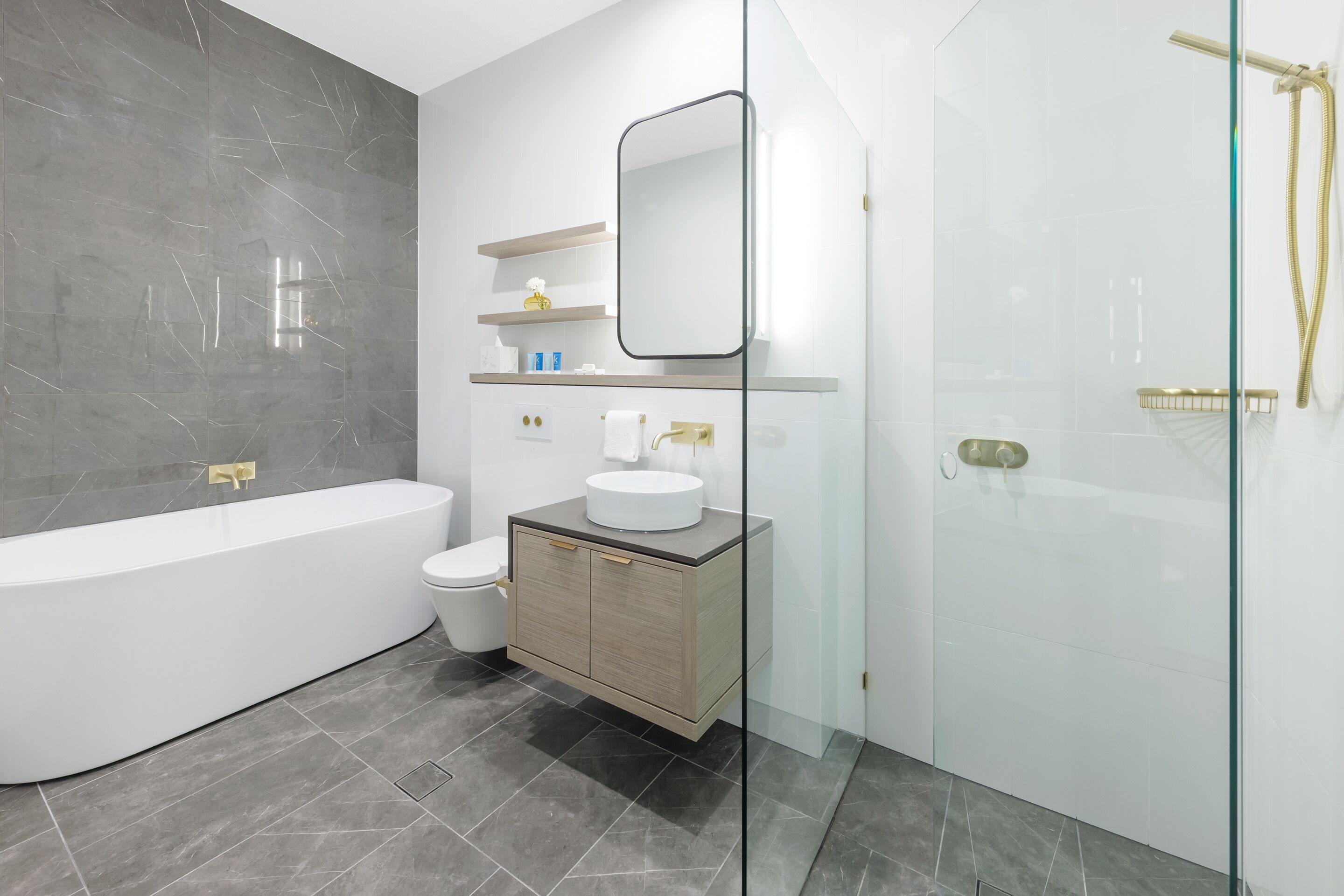 Un baño moderno con una bañera independiente, un inodoro, un tocador con espejo y una zona de ducha con mampara de vidrio.