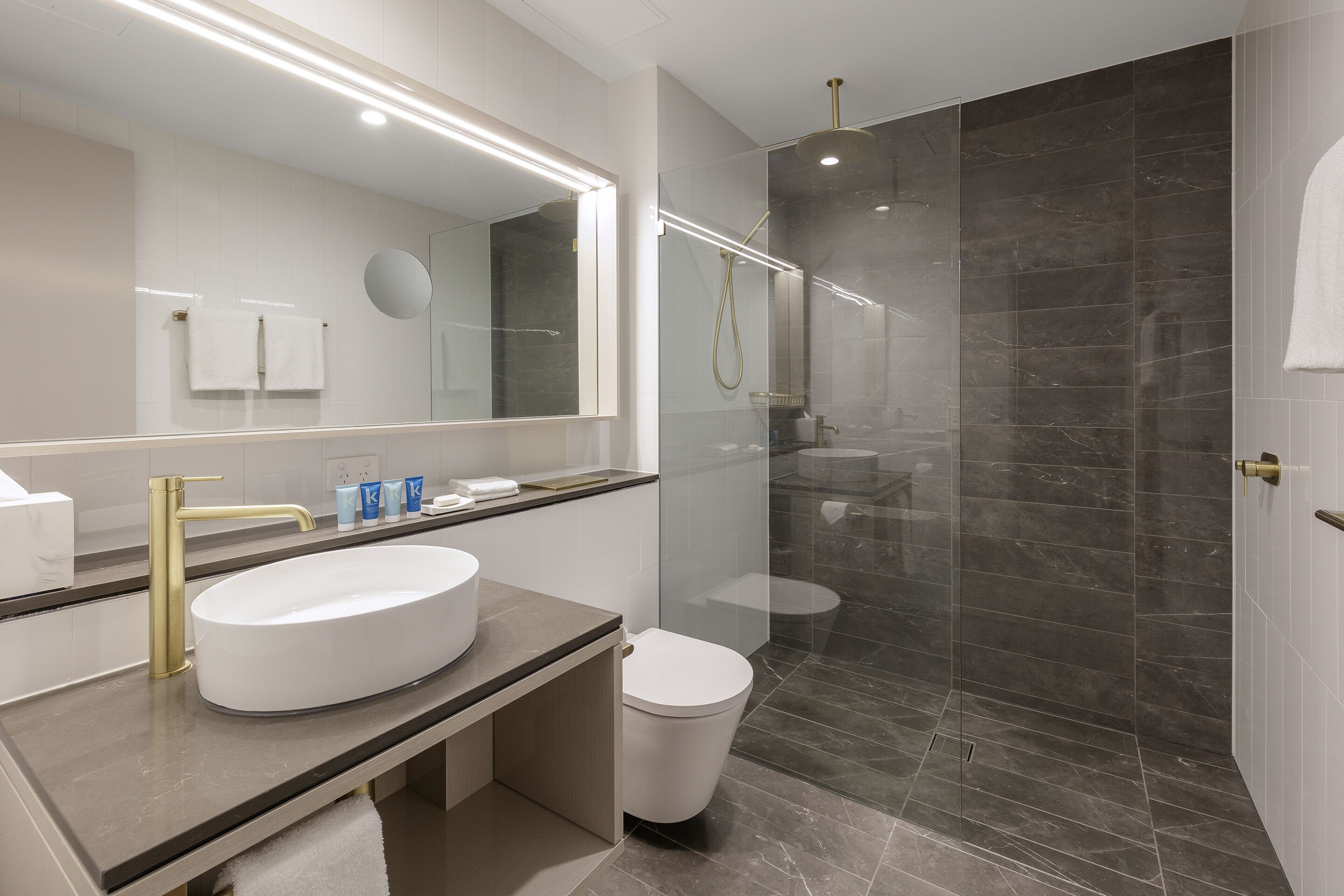 A modern bathroom with a large mirror, a round sink, a toilet, and a glass-enclosed shower area.