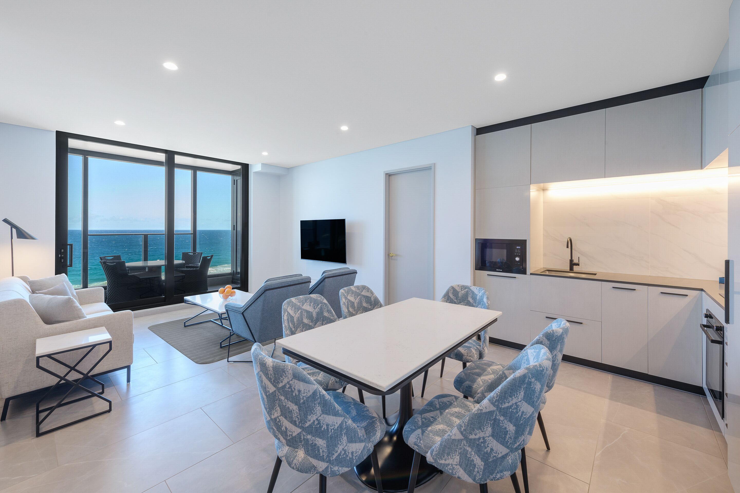 A modern living room with a large window, a dining area, and a kitchen with a built-in oven.