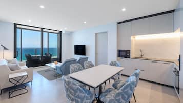 A modern living room with a large window, a dining area, and a kitchen with a built-in oven.