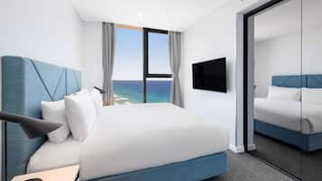 A modern hotel room with a large bed, a flat-screen TV, and a view of the ocean through large windows.