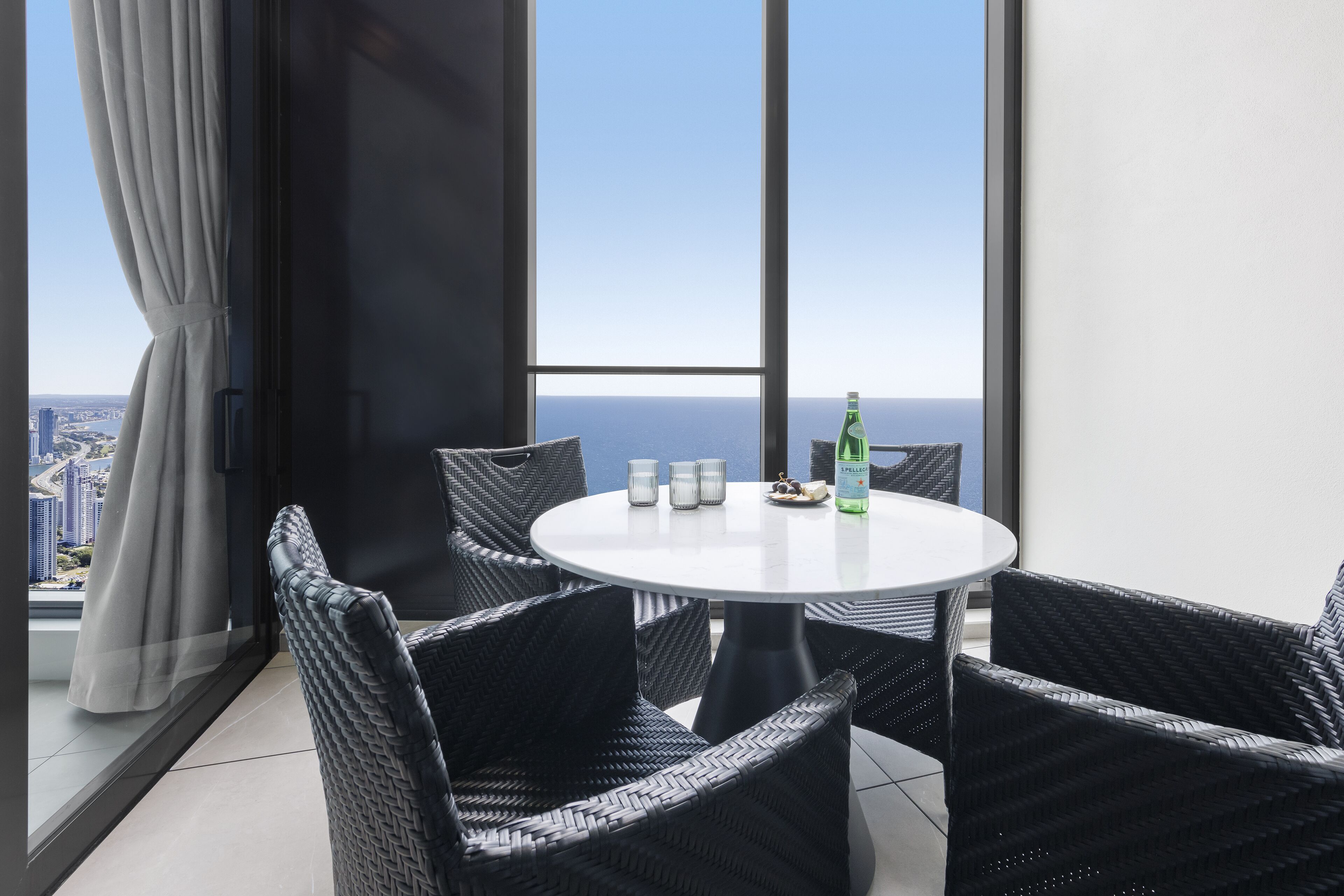 A balcony with wicker chairs, a round table, and a bottle of water.