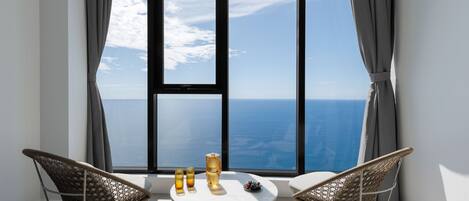 A room with a large window, two wicker chairs, a small round table, and three glasses.