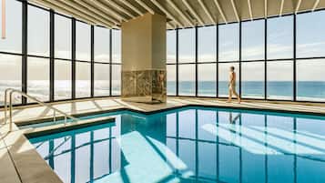 An indoor swimming pool with a view of the ocean through large windows.