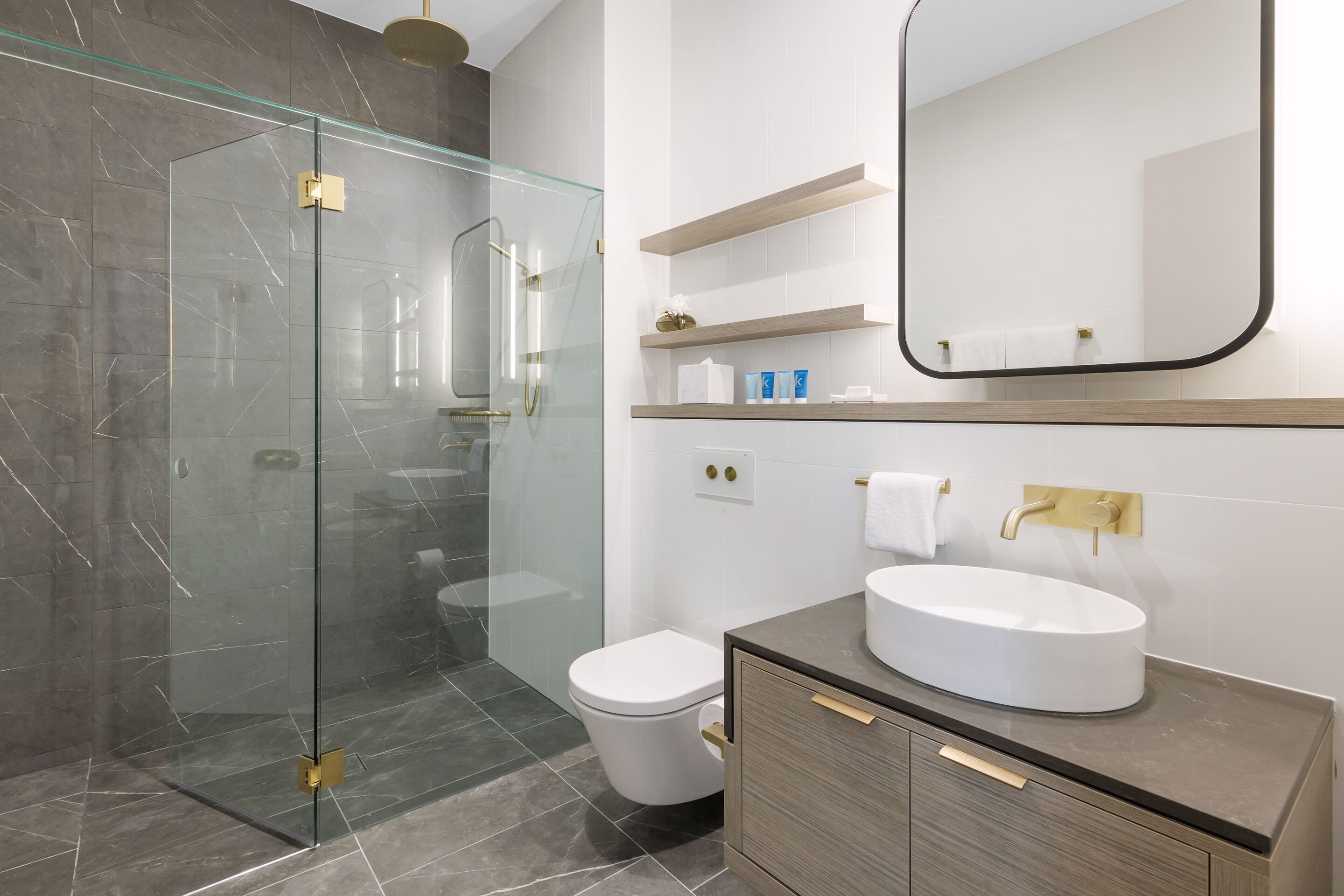 A modern bathroom with a glass-enclosed shower, a white toilet, and a vanity with a round sink.