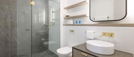 A modern bathroom with a glass-enclosed shower, a white toilet, and a vanity with a round sink.