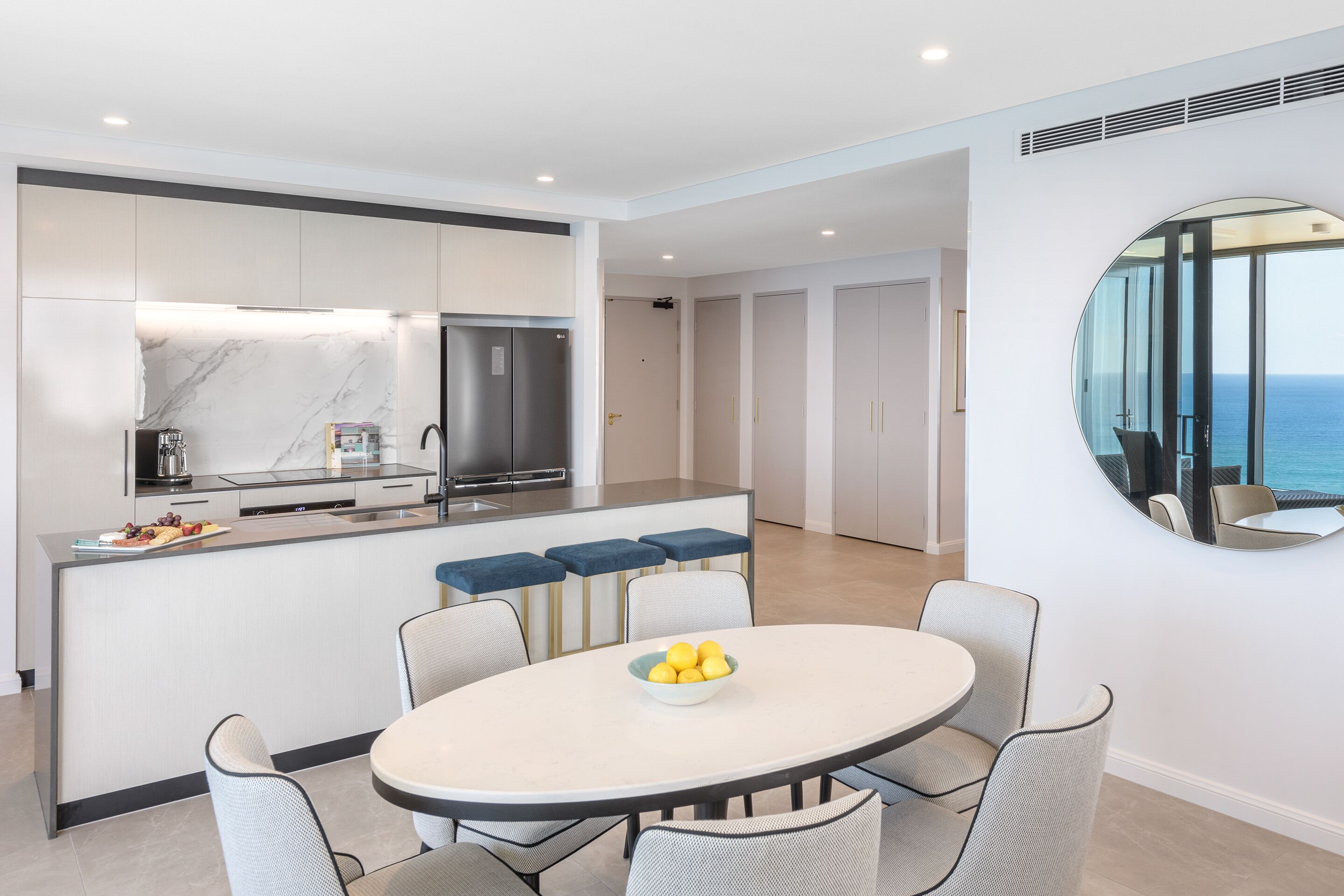 A modern kitchen with a marble backsplash, a central island with bar stools, and a dining area with a round table and chairs.