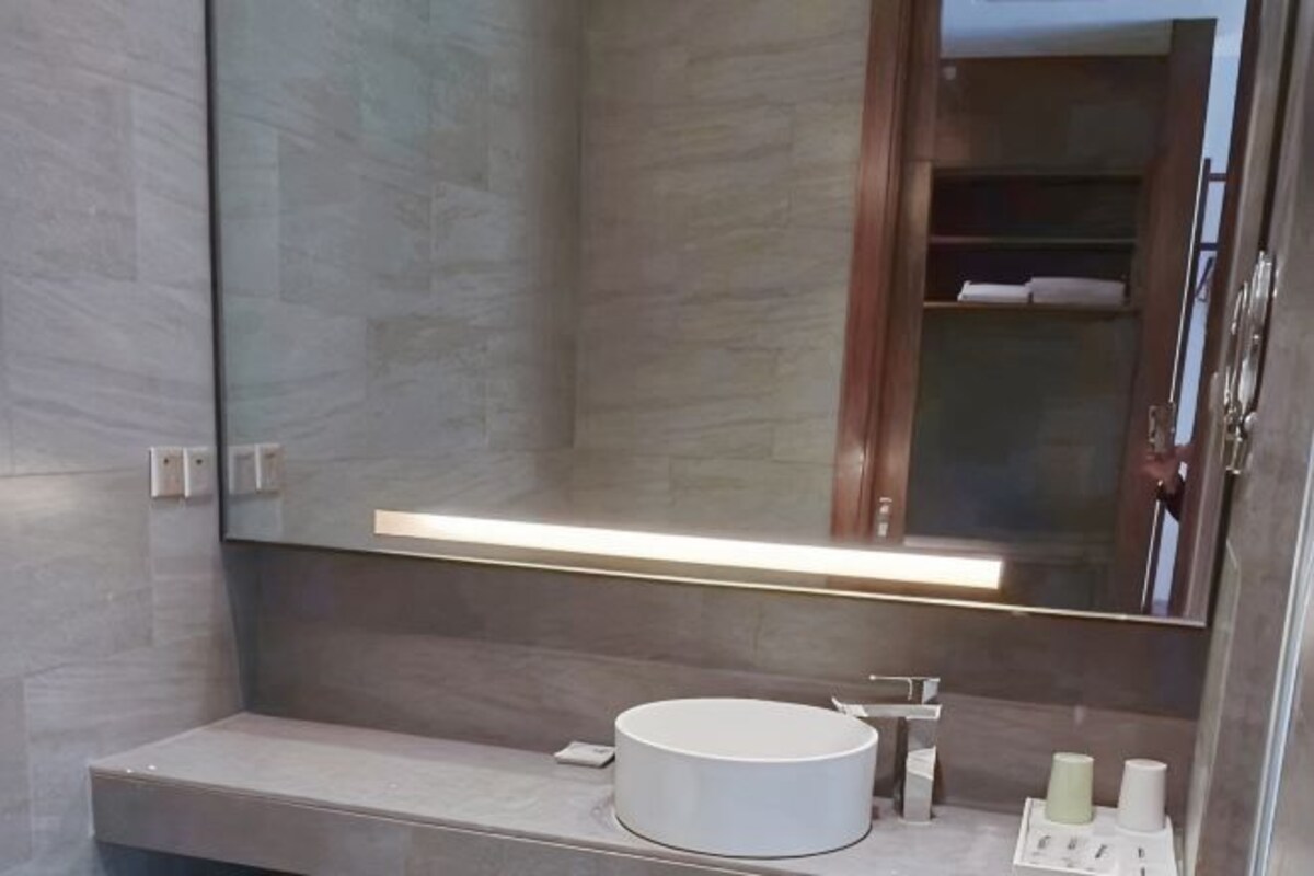 Bany amb un mirall gran, un lavabo rodó i una superfície amb articles de tocador.
