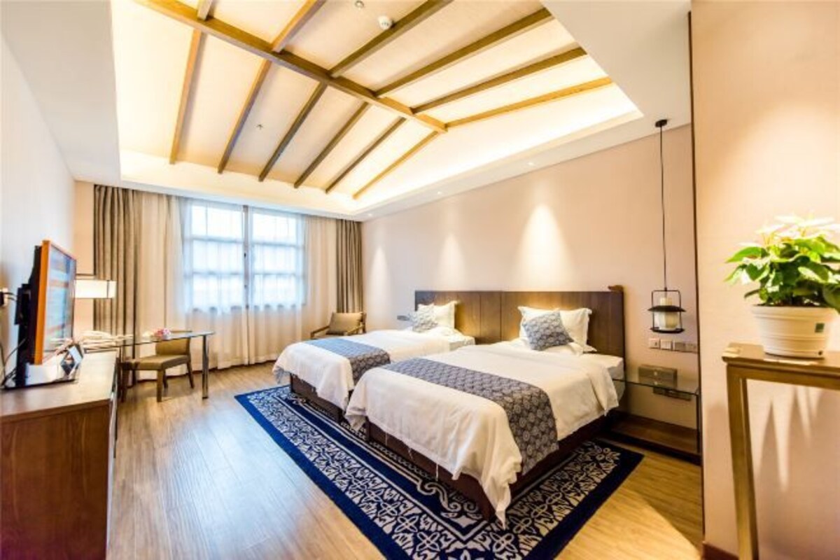 Habitació d'hotel amb dos llits, una taula de treball, una cadira, una finestra gran amb cortines i un sostre amb bigues de fusta.