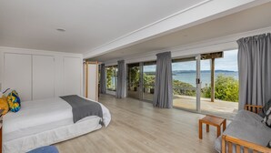 Une chambre spacieuse avec un grand lit, un canapé et une vue sur la mer grâce à de grandes fenêtres du sol au plafond.