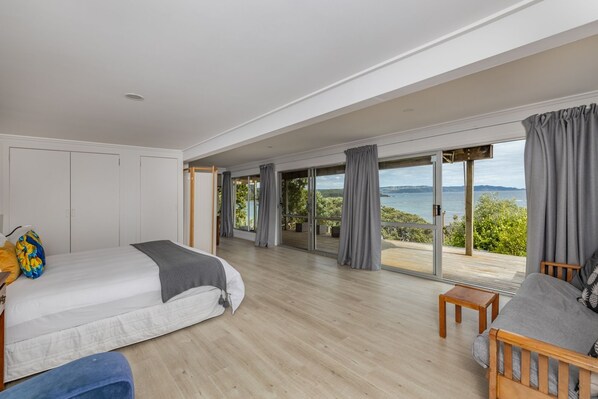 Un dormitorio espacioso con una cama grande, un sofá y vistas al mar a través de ventanas de gran altura.