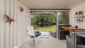 Une terrasse moderne avec une chaise blanche, une table en bois et une porte vitrée donnant sur un jardin.
