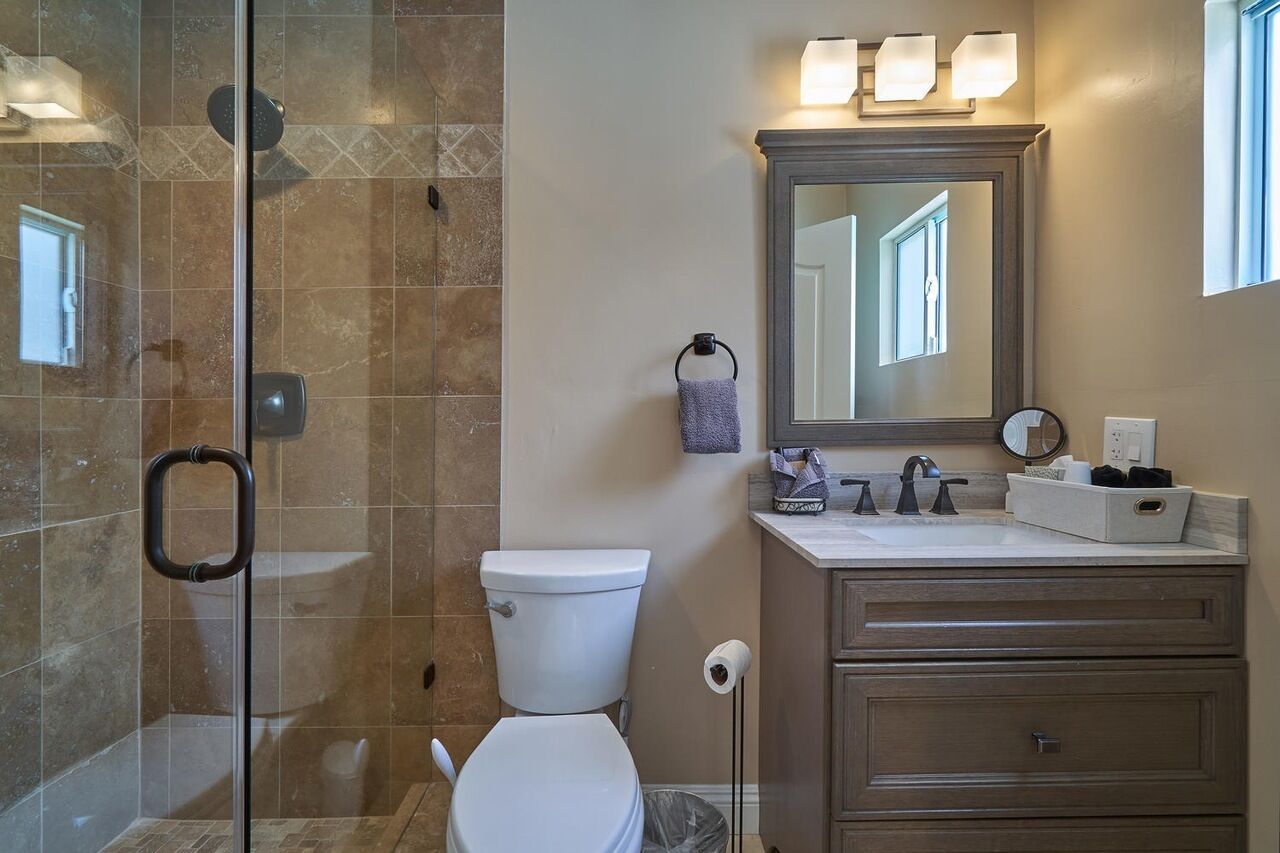 Un bagno con box doccia in vetro, un water, un lavandino con specchio e un mobile contenitore con cassetti.