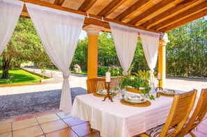 An outdoor dining area with a covered pergola, white tablecloths, and wooden chairs.