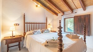 A bedroom with a four-poster bed, wooden headboard, bedside tables with lamps, and a window with a view.