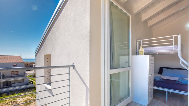 Una habitación con literas, una puerta corredera, un pequeño tocador blanco y vista al mar.